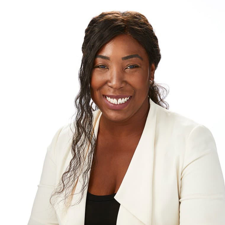 Smiling Black woman with long wavy hair wearing a white blazer over a black top.